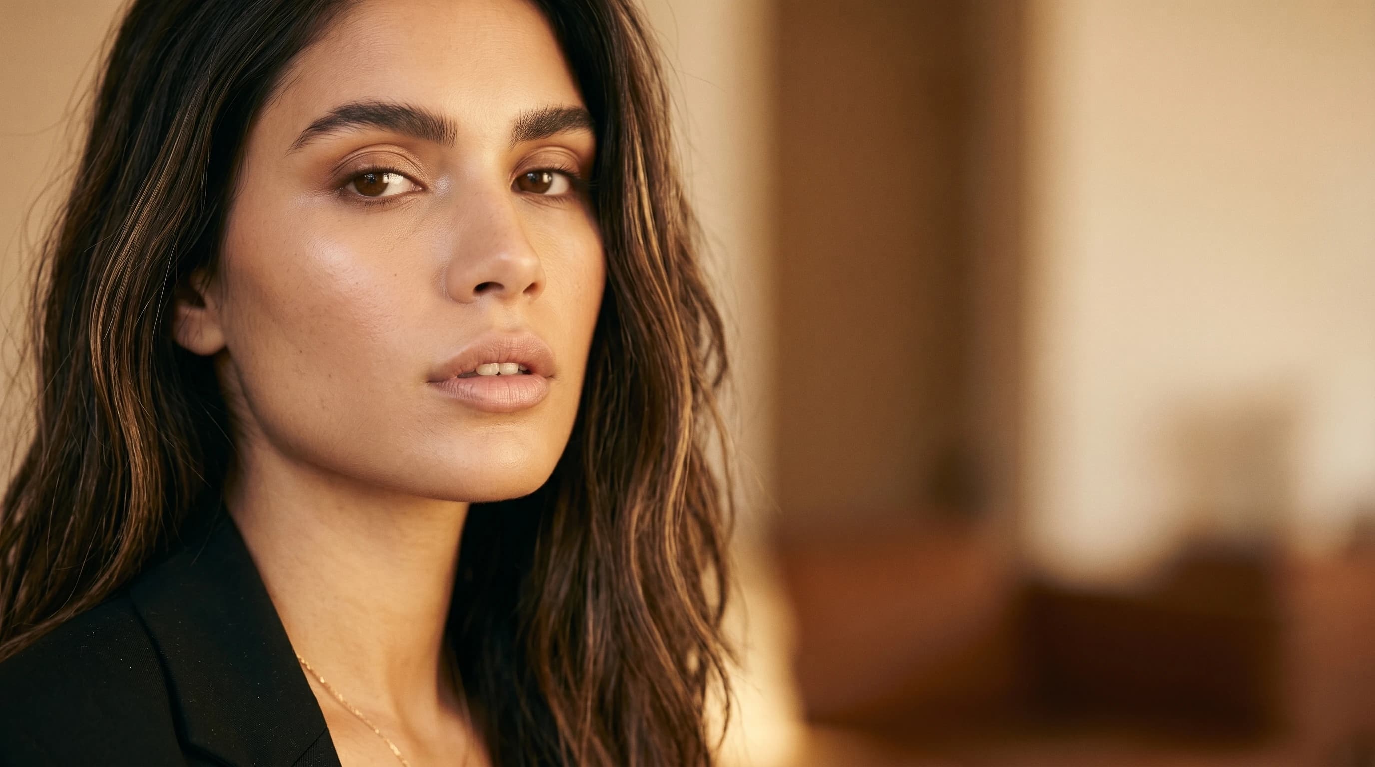 Editorial Beauty-Porträt einer jungen Frau mit ruhiger Lippen- und Kinnpartie in elegantem schwarzem Blazer, warmes Fensterlicht — Lippenfiller, Praxis Ästhetik am Isartor München