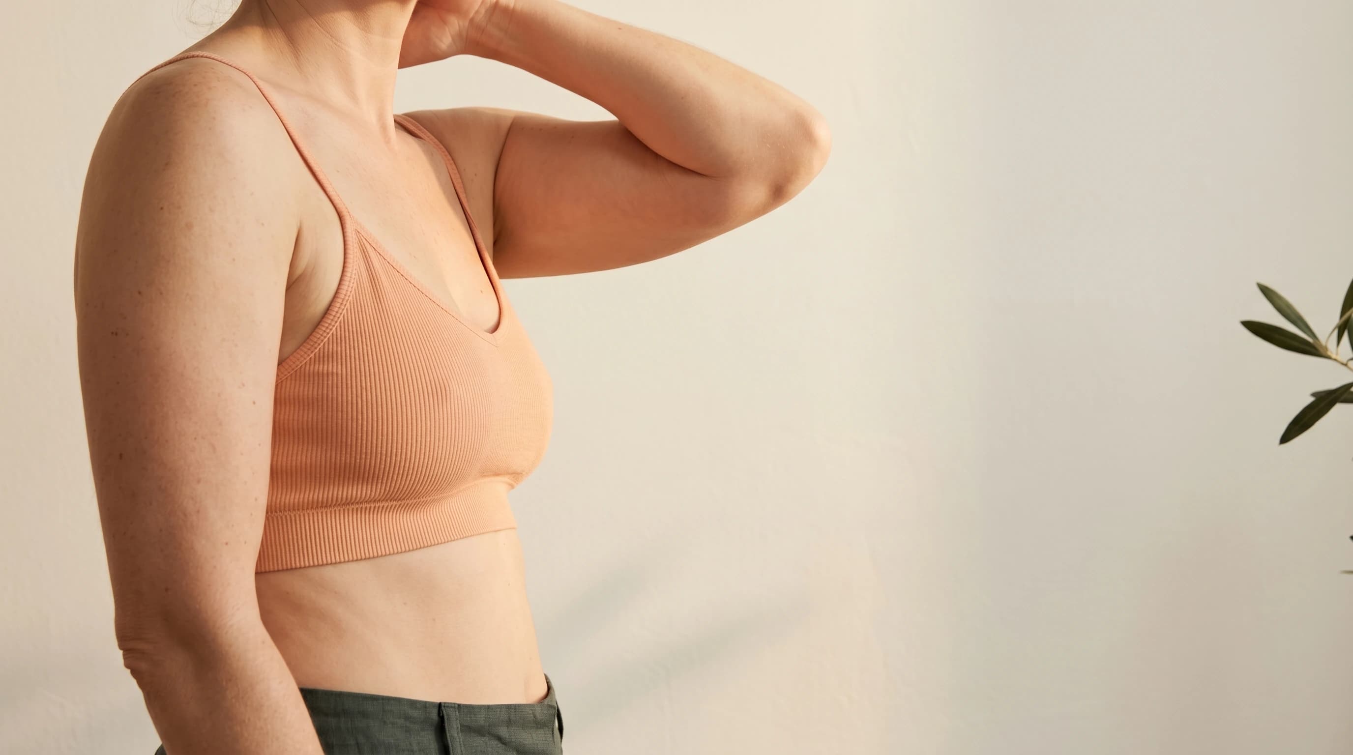 Editorial Oberkörper in peach Strick mit angehobenem Arm — natürliche Kontur der Oberarm-Innenseite. Praxis Ästhetik am Isartor München