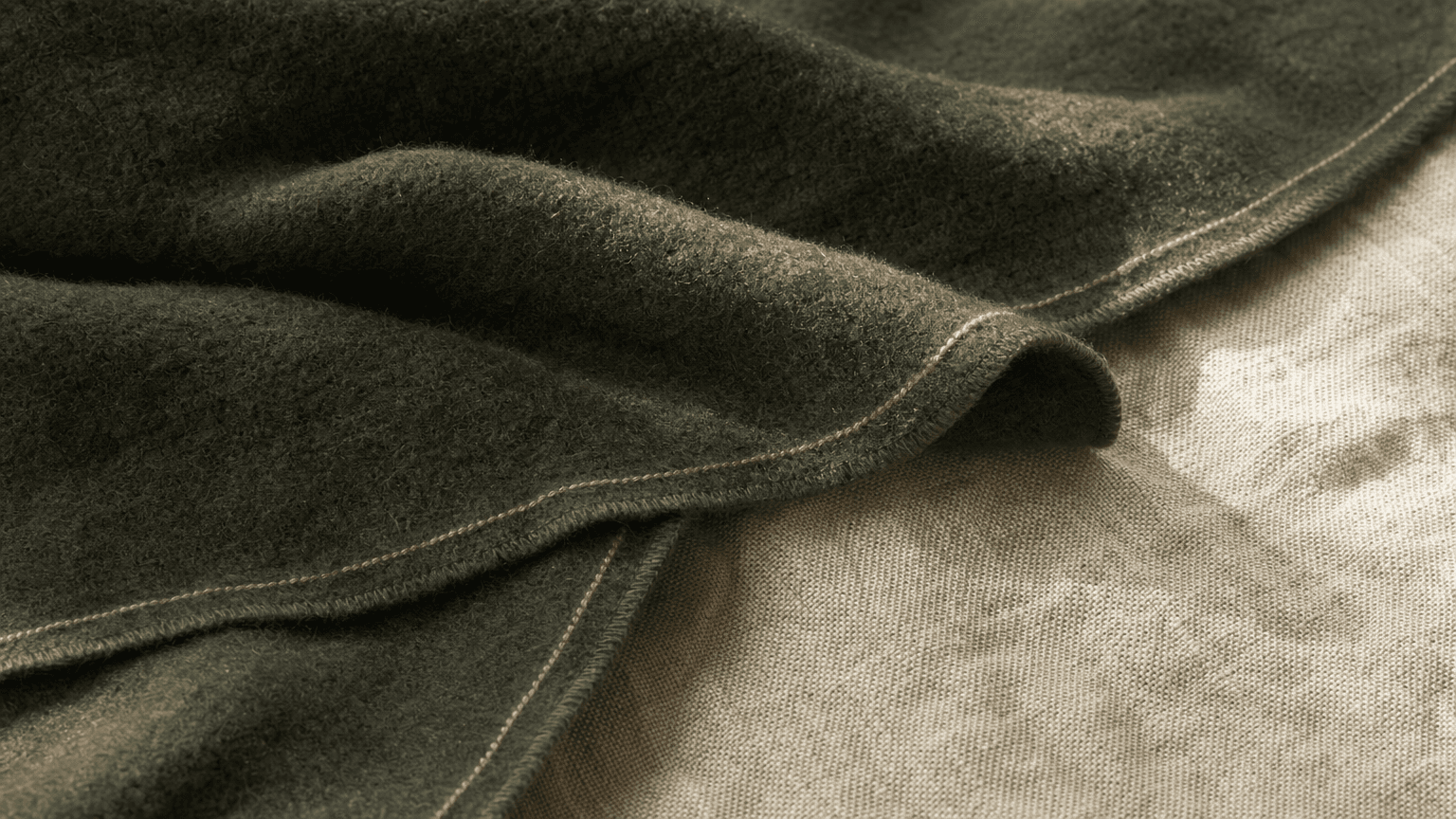 Charcoal-forest Wolldecke mit peach Hairline-Trim auf bone-cream Linen — ruhige, warme Recovery-Textur